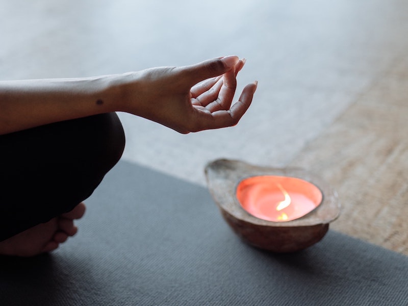 We see a hand and toes and the thumb and the middle finger are touching. We see an object like a cup which has a flame in it. It looks like this person is meditating