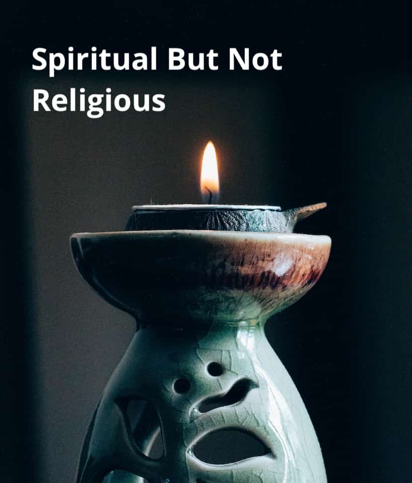 A votive candle burns in a grey-blue ceramic holder. The words "Spiritual but not religious" are seen above the candle.