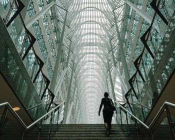 A woman is going up the stairs. The photo is taken from downstairs, so we look at her from below. It looks like there's a long corridor after the stairs.