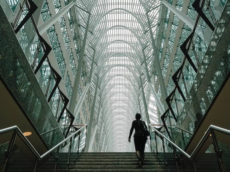 A woman is going up the stairs. The photo is taken from downstairs, so we look at her from below. It looks like there's a long corridor after the stairs.