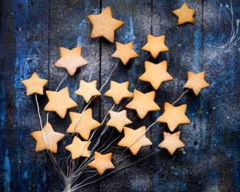 A spray of of 20 gold star shapes attached to a branch-shaped wire. The background appears to be wood painted dark blue and sparkly silver.