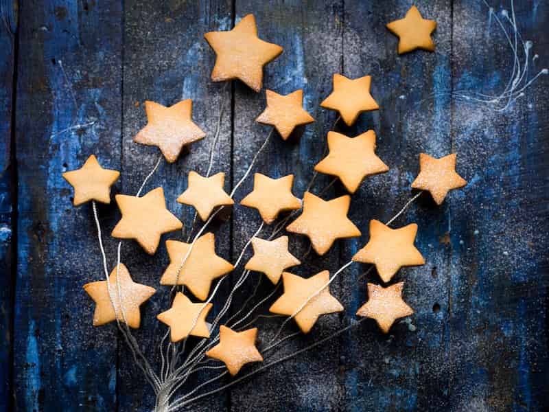 A spray of of 20 gold star shapes attached to a branch-shaped wire. The background appears to be wood painted dark blue and sparkly silver.