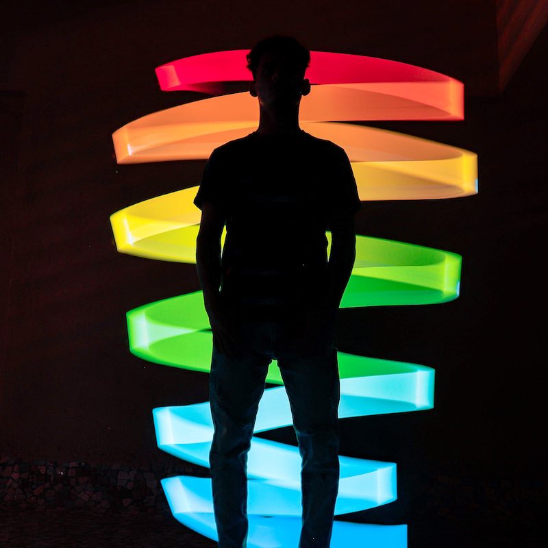 A figure of a person is silhouetted in front of a large spiral of multi-color light. The background is dark and the colors of the spiral are luminous.