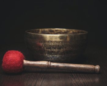 A beautiful bronze singing bowl sits on a table, a soft mallet resting in front of it.