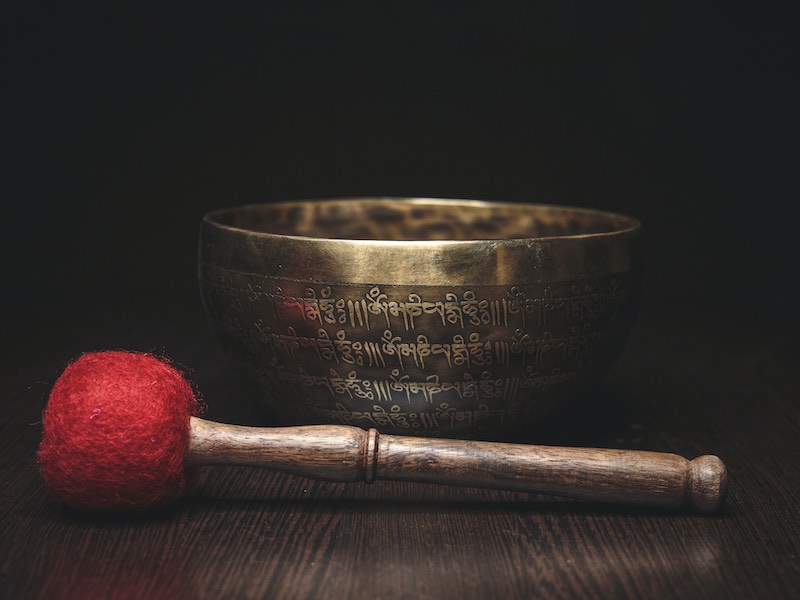 A beautiful bronze singing bowl sits on a table, a soft mallet resting in front of it.